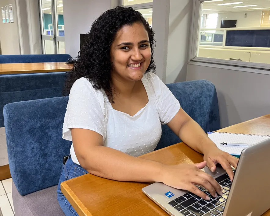 Jovem estagiária sorrindo sentanda em uma mesa no escritório