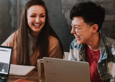 Dois jovens sorrindo enquanto estão estudando juntos utilizando jalecos brancos semelhantes aos de medicos e cientistas