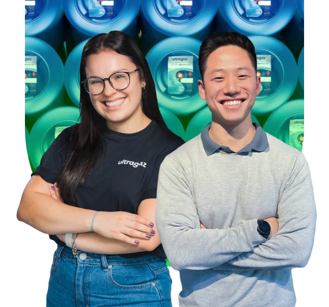 Casal de jovens estágiarios com um lindo sorriso. O jovem esyágiario está utilizando uniforme nas cores azul e cinza com o logo da Ultragaz. Enquanto isso a jovem estágiaria está usando uma roupa social preta.